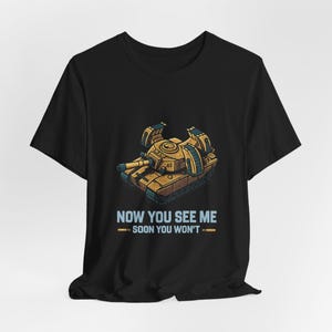May include: Black t-shirt featuring a cartoon tank in shades of tan and brown. The text "NOW YOU SEE ME SOON YOU WON'T" is printed in blue below the tank illustration. The shirt is made of a soft material.