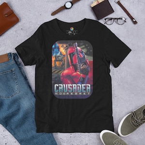 May include: Black t-shirt featuring a graphic of a red-armoured character holding a gun. The graphic includes the text "CRUSADER NO REGRET".