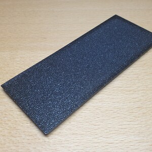 May include: A black rectangular sanding block with a textured surface.