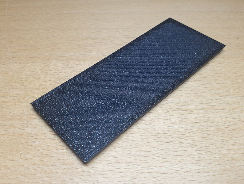 May include: A black rectangular sanding block with a textured surface.