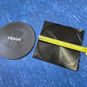 May include: Two black circular discs, one measuring 160mm in diameter, next to a larger black disc with a measuring tape showing a diameter of 160mm.