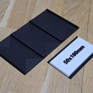 Pode incluir: Um suporte de exibição preto dobrável de três painéis com um rótulo branco que diz "50x100mm".