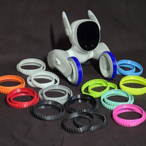 May include: A white robot dog with blue wheels and a black screen. The robot is surrounded by a variety of colorful rubber rings.