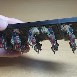 May include: A set of 10 green and red painted miniature figures of goblins holding weapons, mounted on a black plastic base. The figures are arranged in a row and are ready for battle.