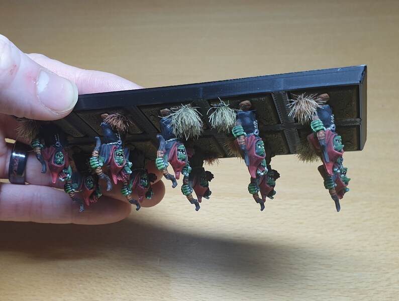 May include: A set of 10 green and red painted miniature figures of goblins holding weapons, mounted on a black plastic base. The figures are arranged in a row and are ready for battle.