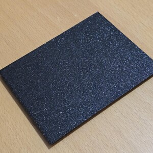 Op de afbeelding: Een zwarte, textuurkaart met een fijne glitterafwerking.