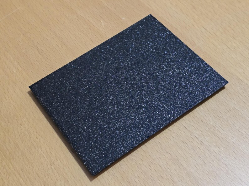 Op de afbeelding: Een zwarte, textuurkaart met een fijne glitterafwerking.