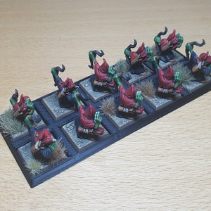 May include: A set of ten green and red goblin miniatures, each with a red hood and a weapon, standing on a black base with brown grass.