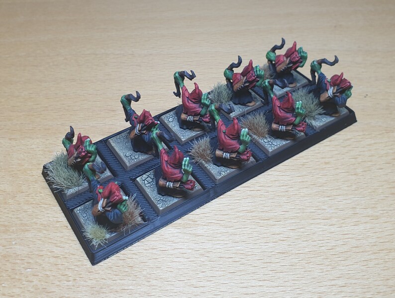 May include: A set of ten green and red goblin miniatures, each with a red hood and a weapon, standing on a black base with brown grass.