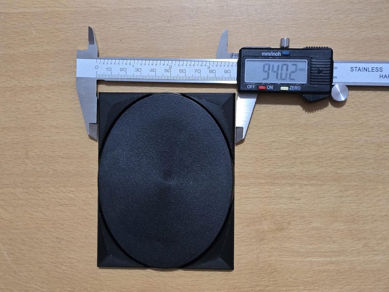 Op de afbeelding: Een zwart rond object van plastic met een diameter van 23,88 cm, gemeten met een digitale schuifmaat.