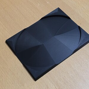 Op de afbeelding: Een zwart 3D-geprint object met een geometrisch ontwerp. Het object heeft een reeks concentrische cirkels en lijnen die een patroon cre&euml;ren.
