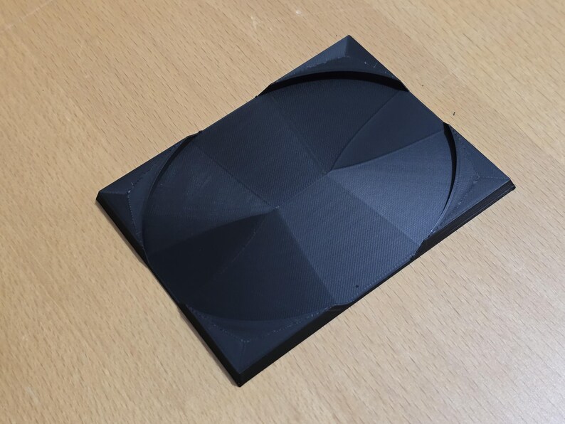 Op de afbeelding: Een zwart 3D-geprint object met een geometrisch ontwerp. Het object heeft een reeks concentrische cirkels en lijnen die een patroon cre&euml;ren.