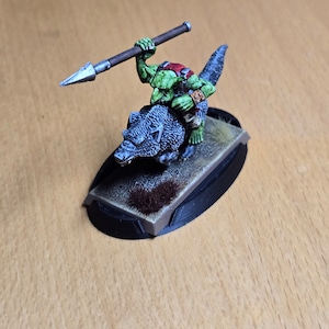 May include: A green Orc riding a gray wolf with a silver spear. The miniature is painted and mounted on a black base.