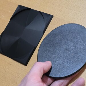 Op de afbeelding: Twee zwarte, ronde, getextureerde, 3D-geprinte objecten. Een object is plat en het andere is een verhoogd, geometrisch ontwerp.
