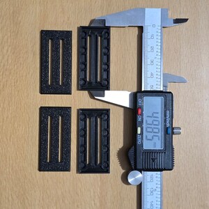 May include: Four black plastic pieces with different patterns of holes. A digital caliper measures the width of one of the pieces at 49.85 mm.