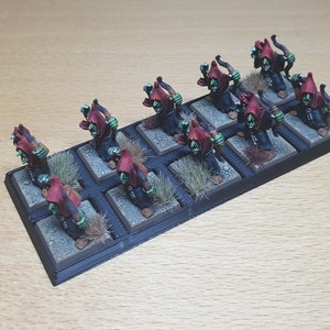 May include: A set of 12 green and red painted miniature figures of orcs with bows and arrows, standing on a black base with brown grass tufts.