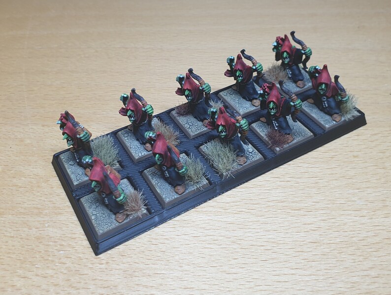 May include: A set of 12 green and red painted miniature figures of orcs with bows and arrows, standing on a black base with brown grass tufts.
