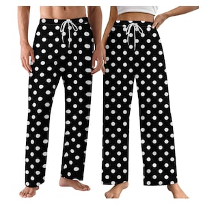 Puede incluir: Pantalones de pijama negros con un estampado de lunares blancos. Los pantalones tienen cintura con cordón. La imagen muestra los pantalones en dos personas.