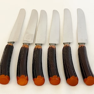 May include: Set of six stainless steel dinner knives with brown and orange handles. The knives have a simple, classic design.