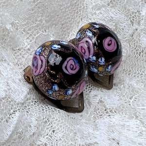 May include: A pair of black glass earrings with a floral pattern in pink, blue, and gold. The earrings are round and have a shiny finish.