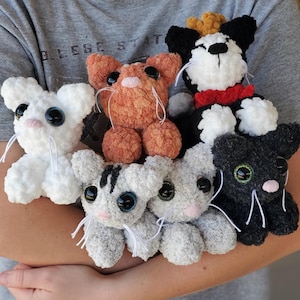 Puede incluir: Una colección de peluches de gatos hechos a mano con ganchillo en varios colores, incluyendo blanco, naranja, gris y negro. Cada peluche tiene ojos grandes y expresivos y bigotes blancos. Los gatos son suaves y tiernos.
