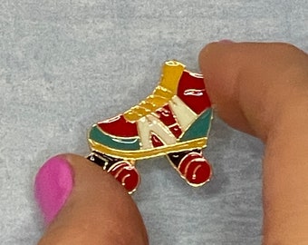 Könnte beinhalten: Eine goldfarbene Rollschuh-Anstecknadel mit roten, weißen und blauen Emaildetails. Der Rollschuh hat eine gelbe Zunge und Schnürsenkel.