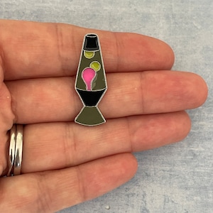 Könnte beinhalten: Eine silberfarbene Lavalampe-Anstecknadel mit grünem Sockel, schwarzem Kopf und rosa und gelbem Wachs im Inneren.