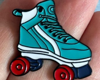 Könnte beinhalten: Türkisfarbene Rollschuh-Anstecknadel mit roten Rollen und weißen Akzenten. Die Nadel hat schwarze Schnürsenkel und einen marineblauen Sockel. Dieser Emaille-Pin ist ein lustiges Accessoire für Rollschuhfans.