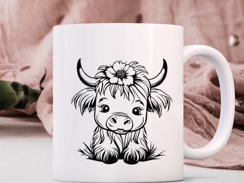May include: White ceramic mug with a black and white illustration of a Highland cow with a flower on its head.
