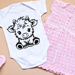 May include: A white baby onesie with a black and white illustration of a cartoon cow. The onesie has short sleeves and a snap closure at the bottom.