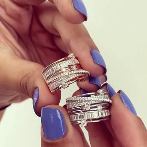 May include: Two stackable rings with multiple bands of clear cubic zirconia stones. One ring has a rose gold band and the other has a silver band.