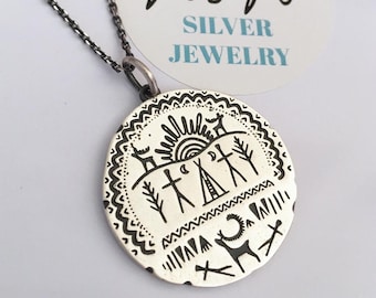 May include: A silver pendant necklace with a detailed, etched design. The round pendant features a sun, figures, and animals. The necklace chain is dark gray. The pendant is stamped with the text "N&N SILVER JEWELRY".