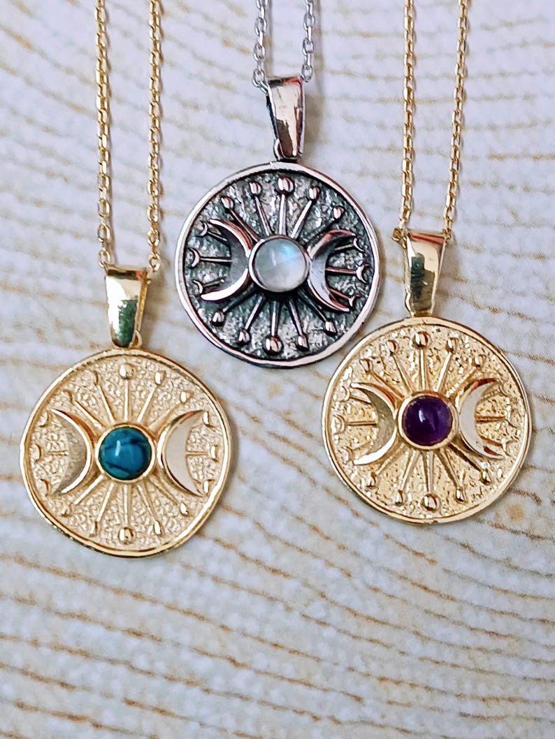 May include: Three celestial-themed necklaces. Two are gold-toned, featuring a central stone and crescent moon design. The third is silver-toned with a similar design and a central stone. All have delicate chains.
