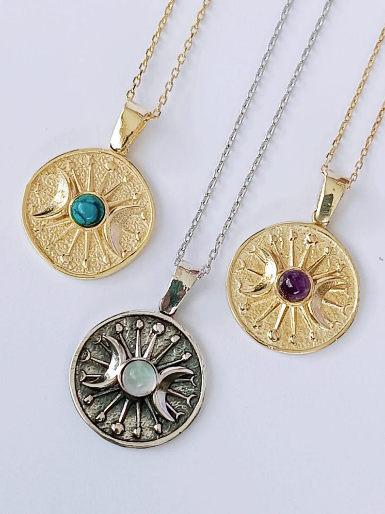 May include: Three celestial-themed pendant necklaces. Two are gold-toned, one with a turquoise stone and the other with an amethyst. The third necklace is silver-toned with a pearlescent stone. Each pendant features a sun, moon, and star design.