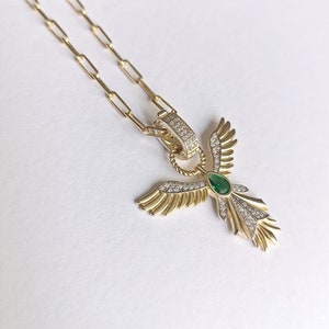 Pode incluir: Um colar de corrente de ouro com um pingente que apresenta um anjo estilizado com asas, uma gema verde e pedras brilhantes transparentes.