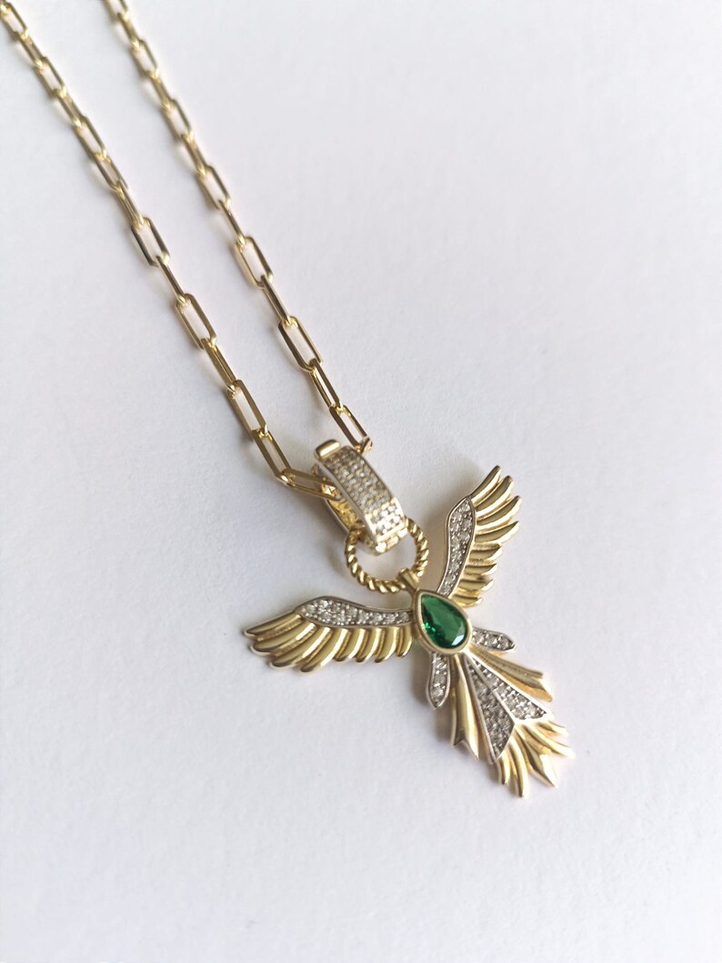 Pode incluir: Um colar de corrente de ouro com um pingente que apresenta um anjo estilizado com asas, uma gema verde e diamantes pav&eacute;.