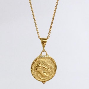 K&ouml;nnte beinhalten: Eine goldene Kettenkette mit einem runden Anh&auml;nger, der ein detailliertes Profil eines Frauenkopfes mit einer Krone zeigt. Der Anh&auml;nger ist mit kleinen, klaren Steinen verziert.
