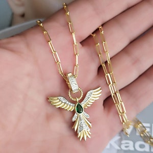 Pode incluir: Colar de corrente dourada com um pingente em forma de p&aacute;ssaro alado com uma gema verde e strass transparentes.