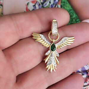 Pode incluir: Pingente de ouro com uma gema verde e strass transparentes em forma de um p&aacute;ssaro estilizado com as asas abertas.