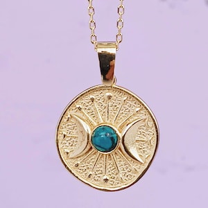 May include: Gold-colored pendant necklace featuring a circular pendant with a turquoise stone center and crescent moon designs. The pendant is suspended from a delicate chain. The necklace has a celestial or spiritual theme.