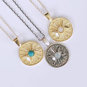 May include: Four necklaces with circular pendants. Two pendants are gold-toned, one with a turquoise stone and the other with a white stone. The third pendant is silver-toned with a light blue stone. The fourth pendant is gold-toned with a white stone.