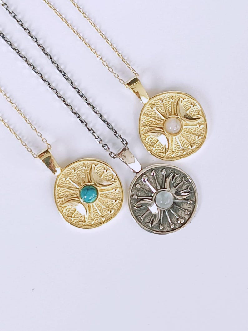 May include: Four necklaces with circular pendants. Two pendants are gold-toned, one with a turquoise stone and the other with a white stone. The third pendant is silver-toned with a light blue stone. The fourth pendant is gold-toned with a white stone.