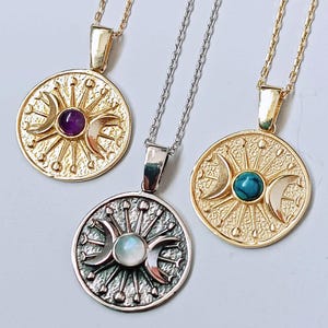 May include: Three necklaces with circular pendants. Two are gold-toned, one with an amethyst and the other with a turquoise stone. The third necklace is silver-toned with a moonstone. Each pendant features a sunburst design with crescent moons.