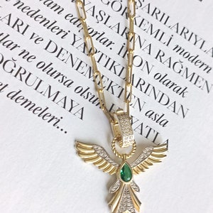 Pode incluir: Um colar de corrente de ouro com um pingente que apresenta um anjo alado com uma gema verde e detalhes de diamantes.