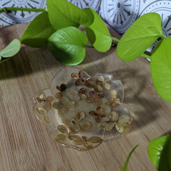 Plat de bibelots dorés au miel et aux fleurs - véritables hortensias séchés en résine transparente sur une base jaune avec des paillettes hexagonales dorées