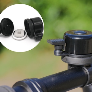 Op de afbeelding: Een zwarte fietsbel met een zilveren ring en een zwarte hendel. De bel is gemonteerd op een zwart stuur.