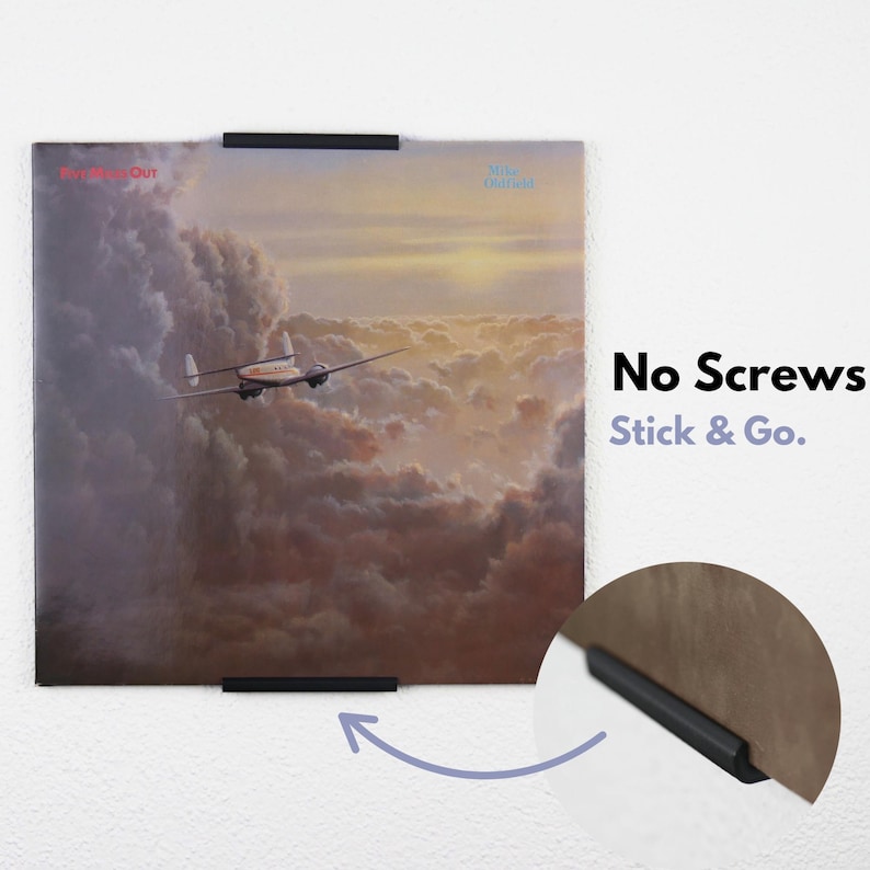 May include: A black vinyl record holder with a record on the wall. The holder is attached to the wall with adhesive strips. The text on the wall reads "No Screws Stick & Go."