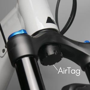 Op de afbeelding: Close-up van een zwarte fietsvork met blauwe accenten. De vork heeft een zwarte luchtventielkap met de tekst "AirTag" eronder.