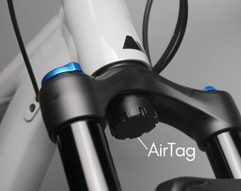 May include: Close-up of a black bicycle fork with blue accents. The fork has a black air valve cap with the text "AirTag" written below it.