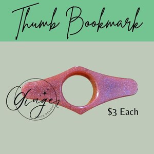 May include: A pink glitter thumb bookmark with a circular opening. The text "Thumb Bookmark" is at the top, and the text "Ginger Chick Designs" is on the left side.